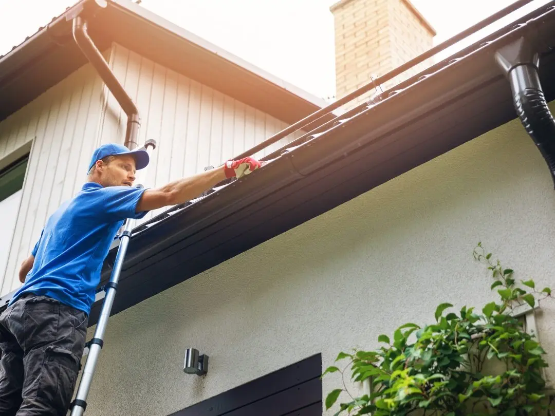 Worker on a ladder clearing a blocked gutter and downpipe on a North Brisbane home